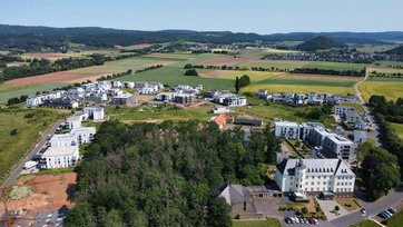 Luftbild im Vordergrund Klostergebebäude. Gelände mit Wiesen, Wäldern, Feldern und viel neuer Wohnbebauung