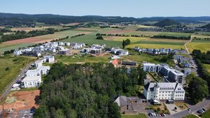 Luftbild im Vordergrund Klostergebebäude. Gelände mit Wiesen, Wäldern, Feldern und viel neuer Wohnbebauung