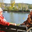 Dame auf Parkbank und Dame im Rollstuhl sitzen sich unterhaltend am Rhein.