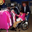 Mädchen im Rollstuhl durchsucht Kleidung, die in einem Laden an der Stange hängt. Mann schiebt den Rollstuhl 