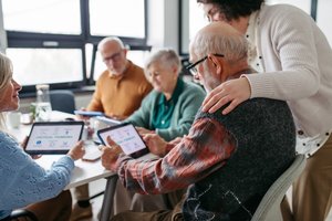 ältere Männer und Frauen sitzen rund um einen Tisch mit Tablets in der Hand
