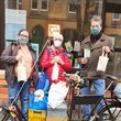 3 Personen mit Mundschutz stehen hinter voll gepacktem Lastenrad und halten Adventstütchen in der Hand.