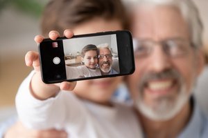 Kleiner Junge sitzt bei seinem Großvater auf dem Schoß und zeigt Selfie, dass er von beiden mit dem Smartphone gemacht hat