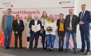 Gruppenfoto mit Menschen auf einer Tribüne, eine Person hält eine Preisurkunde in der Hand