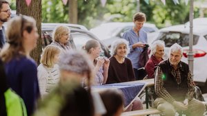 Menschen unterschiedlichen Alters sitzen lachend an einem Tisch am Straßenrand.