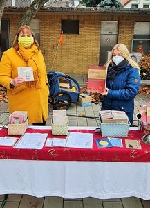 Zwei Frauen mit Mundschutz stehen draußen an einem Bazartisch und verkaufen Weihnachtskarten