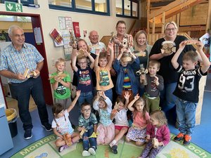 Gruppenfoto mit Kindern, die gebastelte Objekte in die Höhe halten, dabei Männer und Frauen unterschiedlichen Alters