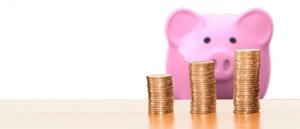 rosa Sparschweindose steht hinter 3 ansteigenden Geldmünzenstapeln auf einem Tisch