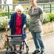 Jüngere Frau begleitet ältere Dame am Rollator auf der Straße