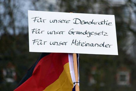 Deutschlandfahne davor ein Pappschild mit der Aufschrift: Für unsere Demokratie, Für unser Grundgesetz, Für unser Miteinander