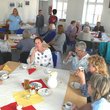 Männer und Frauen unterschiedlichen Alters sitzen an gedeckten Cafétischen und unterhalte sich, im Hintergrund ein Cafébuffet.