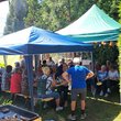 auf zwei Grills liegen Steaks und Würstchen, dahinter sind Zelte aufgebaut in denen Ältere in Sommerkleidung sitzen und stehen