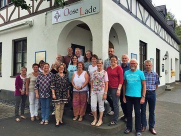 Gruppenbild mit Männer und Frauen vor einem Gebäude mit dem Schild "Oose Lade"
