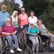 Gruppenfoto im Freien vor Büschen und Bäumen: 3 ältere Damen im Rollstuhl im Vordergund, ein älterer Mann und 3 ältere Frauen im Hintergrund w