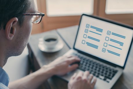 Mann mit Brille sitzt an einem Laptop auf dem Bildschirm sind Umfragekästchen zu sehen