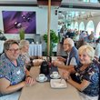 Bild mit älteren Frauen und Männern, die mit Kaffee an mehreren Tischen auf einem Ausflugsschiff sitzen.