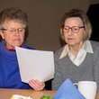Zwei ältere Frauen lesen gemeinsam in einm Text an einer Kaffeetafel