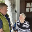 Mann steht lachend mit älterer Frau an deren Haustür.