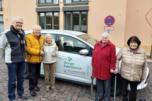 Bild mit einem Ehrenamtlichen Fahrer und drei Seniorinnen und einem Senior, die vor einem PKW stehen, mit dem Aufdruck Bürgerfahrdienst VG Linz