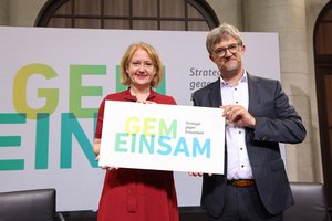 Lisa Paus und Bemjamin Landes halten Schild mit dem Logo "Gem-Einsam" zusammen hoch.