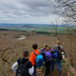 KInder mit Rucksächen stehen an einem Aussichtpunkt mit Geländer und überblicken Wald ohne Laub, einen See und weite Landschaft und Ort am Horizont