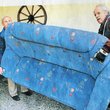 Zwei ältere Männer tragen ein blaues Sofa einer älteren Frau.
