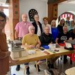Gruppenbild mit zwölf Frauen und Männern, die an einem Tisch mit Nähmaterial und anderen Reparatur-Utensilien sitzen.