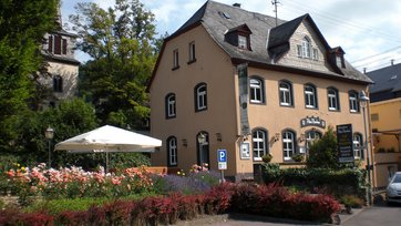 Bild mit altem schiefergedeckten Gebäude, davor ein Rosengarten mit Sonnenschirm