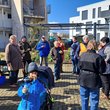 Bild mit Jungen und Älteren in bunten Jacken und Mützen, die auf einer Fläche vor Mehrfamilienhäusern stehen und Brote verzehren.