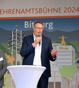 Mann im Anzug und mit Mikrofon auf einer Bühne