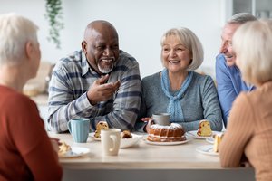 zwei Senioren und drei Seniorinnen sitzen lachend am Tisch mit Kaffeetassen und Kuchen