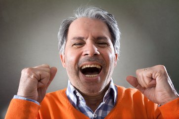Mann im Alter von 60+ mit grauen Haaren, lachend und mit geballten Fäusten