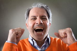 Mann im Alter von 60+ mit grauen Haaren, lachend und mit geballten Fäusten