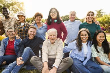 Gruppenfoto von Menschen verschiedenen Alters, die lachend und sich umarmend auf einer Wiese sitzen.