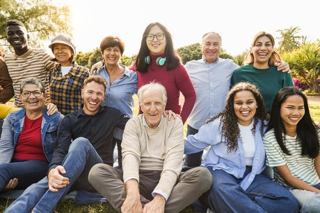 Gruppenfoto von Menschen verschiedenen Alters, die lachend und sich umarmend auf einer Wiese sitzen.
