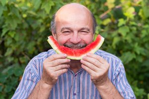 Man mit Schnäutzer hält agbenagte Wassermelonenscheibe vor seinen Mund