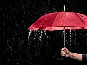 Hand hält rotes Regenschirm vor scharzem Hintergrund, es regnet.