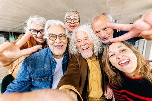 Bild mit einer Gruppe von älteren Männern und Frauen im Ruhestand, die ein Selfiefoto mit dem Handy machen und lachen.