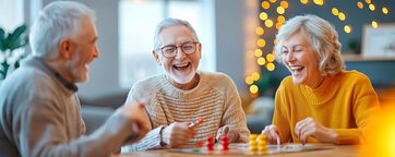Foto mit zwei lachenden Senioren und einer Seniorin, die ein Brettspiel spielen