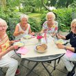 Vier ältere Damen sitzen am Tisch auf einer Terasse, lachen und löffeln Suppe