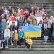 Gruppenfoto von vielen Menschen auf einer Freitreppe, die eine ukrainsche Fahne  in der Mitte halten