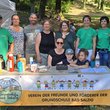 Gruppenbild mit Männer und Frauen mittleren Alters sowie Kindern hinter einem Tisch mit Thermoskannen, Kuchen und Tischkasse