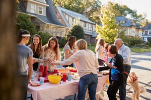 Straßenfest, eine Gruppe von Nachbarn unterschiedlichen Alters stehen um einen Tisch mit Getränken und Speisen