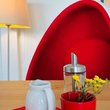 Auschnitt mit rotem bequemen Sessel, rote Tischdekoration mit Milchkännchen und Stehlampe im Hintergrund
