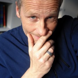 Mann mit blauem Pulli hält Hand am Kinn und grinst